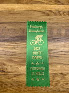 A green ribbon you might see given away at a fair. It reads "DIRTY DOZEN 2022 - OFFICIAL FINISHER"